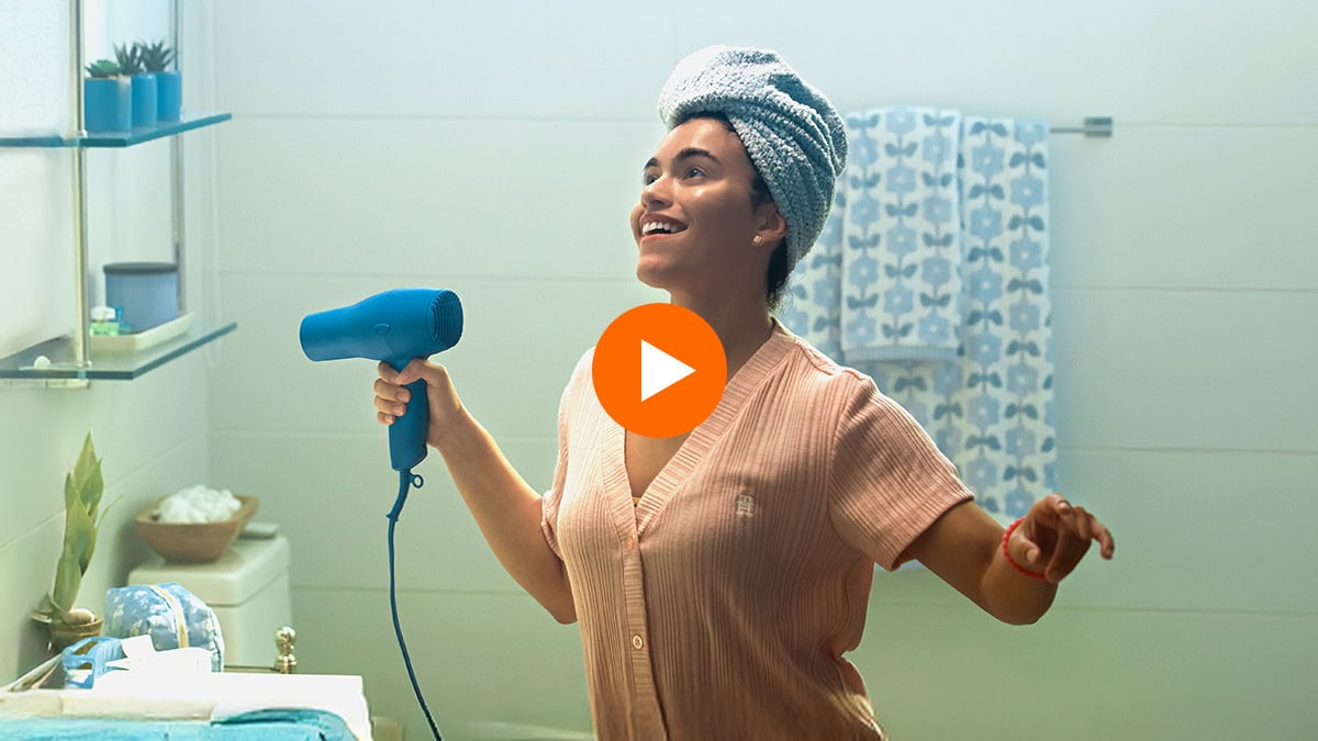 Mujer feliz usando secador de pelo en el baño como parte de su rutina diaria sin interrupciones.